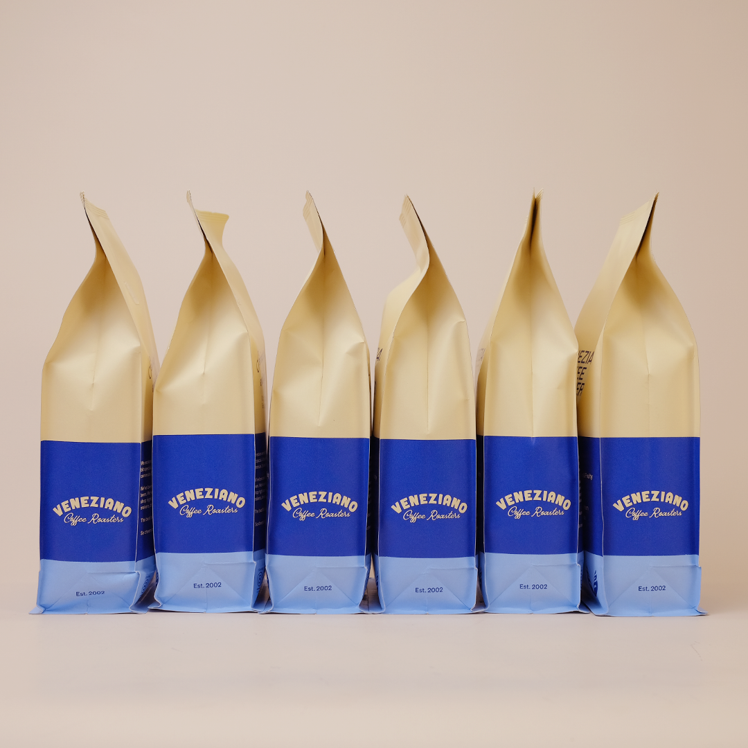 A series of six coffee bags aligned in a row, with a beige upper section and a blue lower section, labeled 'Veneziano Coffee'.