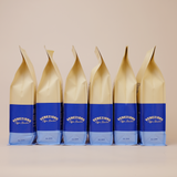 A series of six coffee bags aligned in a row, with a beige upper section and a blue lower section, labeled 'Veneziano Coffee'.